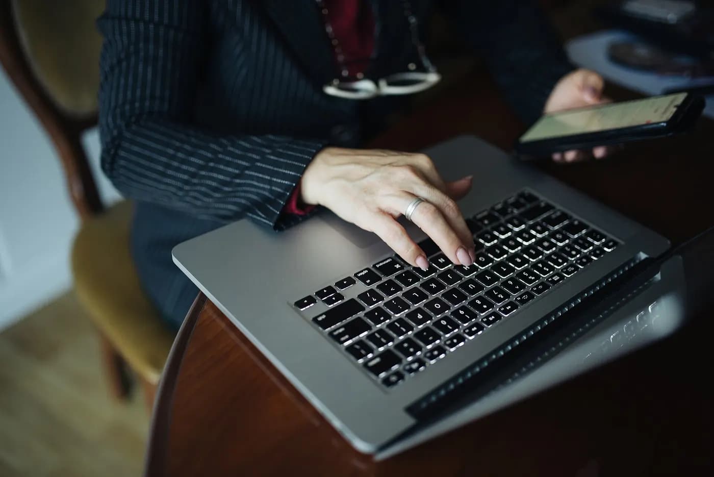 Assistant typing on a laptop with a phone in hand